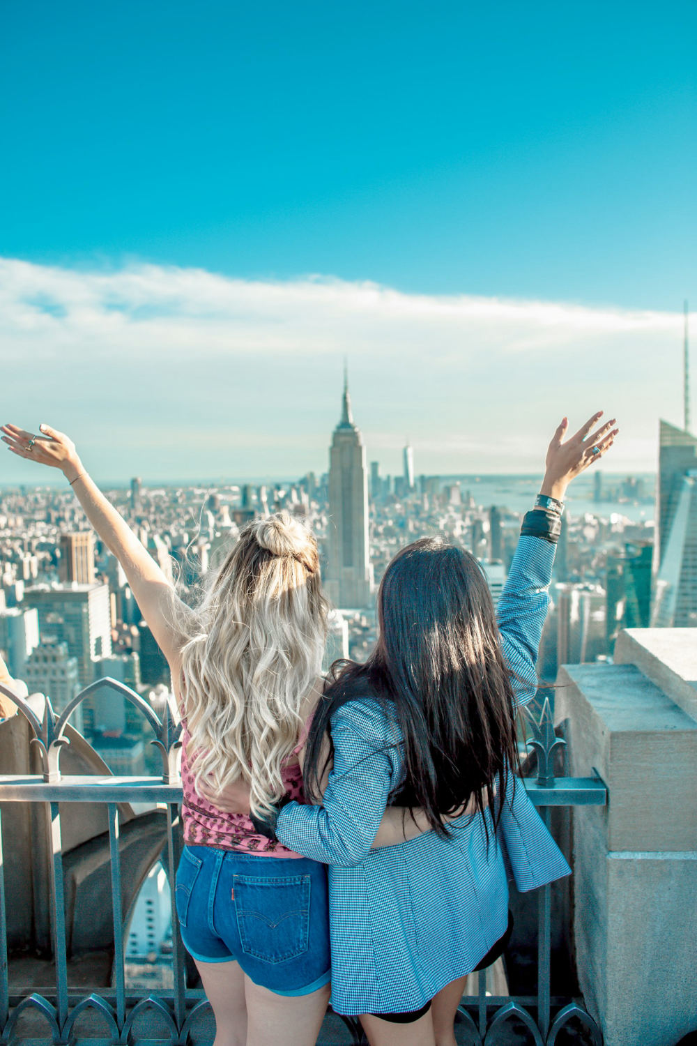 Dos amigas celebrando con los brazos en alto frente al Empire State, en Nueva York