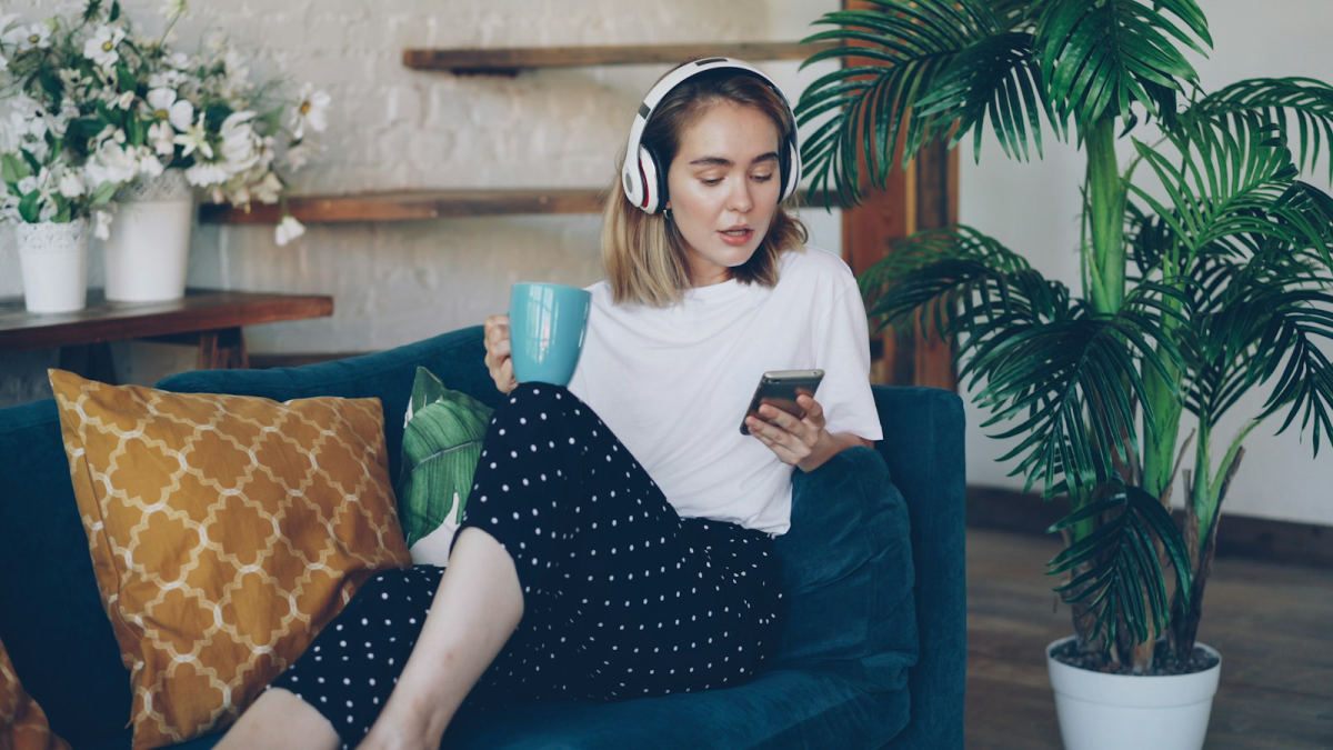 Joven con audífonos y una taza, relajada en el sofá escuchando música